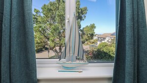 A sailboat model on a windowsill with a view of houses and trees outside.