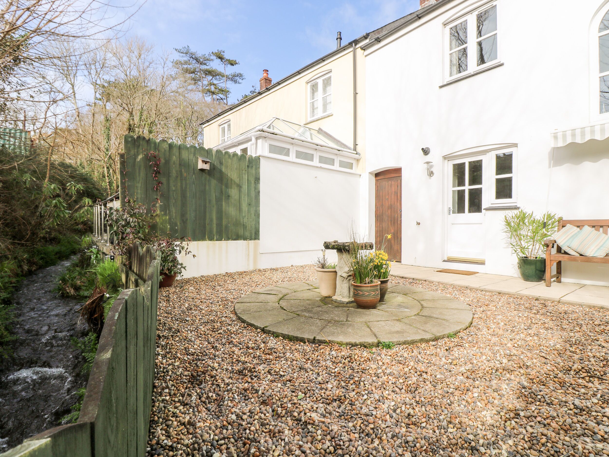 A courtyard with a gravel path, a wooden fence, and a white building with a door and windows.