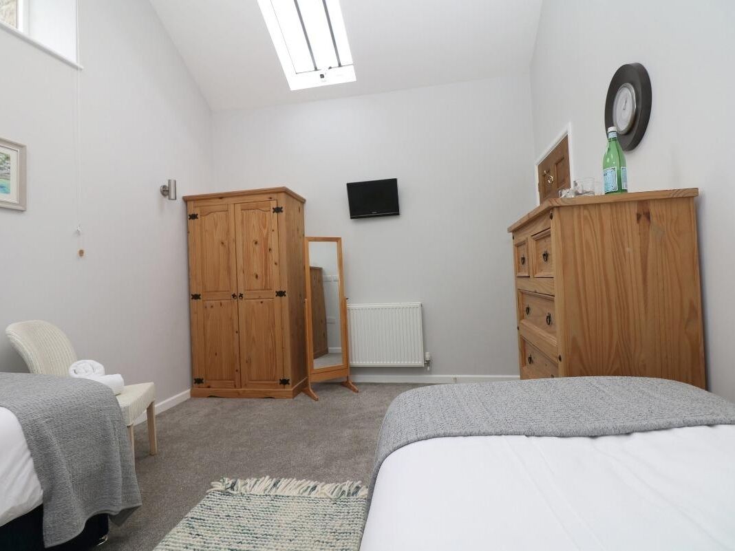 A bedroom with two beds, wooden wardrobes, a television, and a radiator.