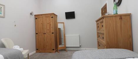 A bedroom with two beds, wooden wardrobes, a television, and a radiator.