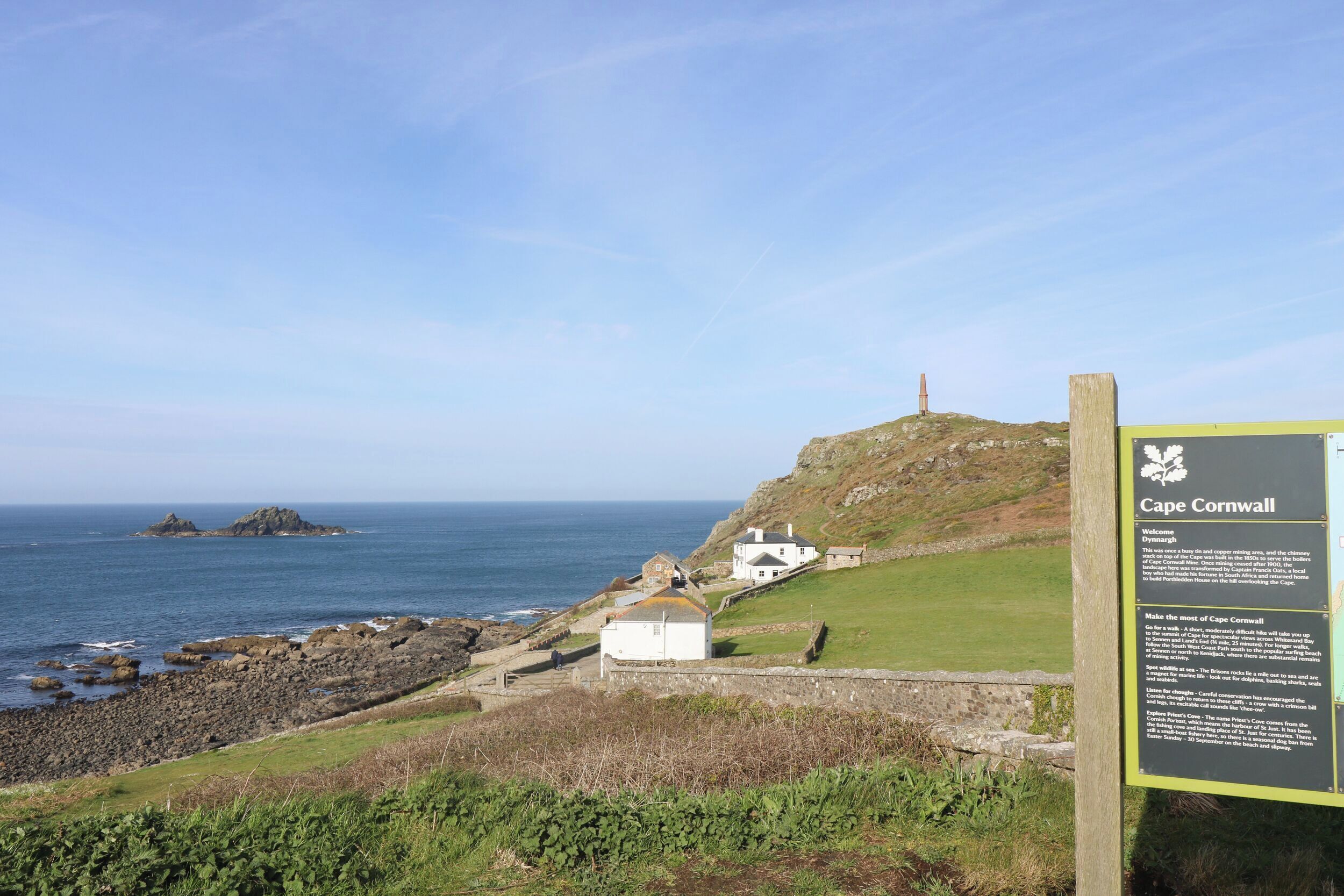 A coastal view with a signboard, rocky shoreline, and a lighthouse.