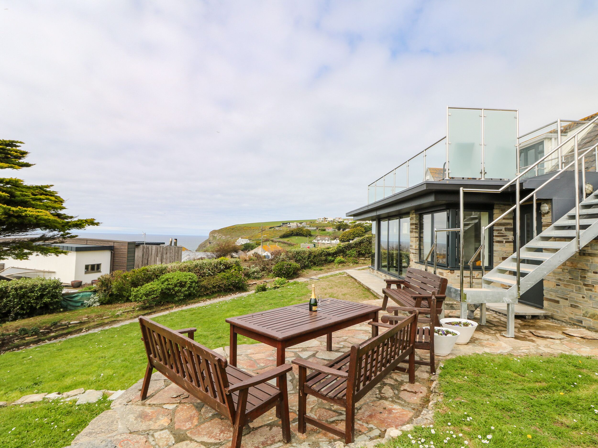 A patio with a table and chairs, a stone pathway, and a view of the sea and hills.