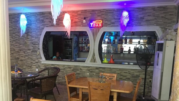 A restaurant with a bar area, wooden furniture, and decorative hanging lights. - Royal Castle Hotel (Lagos)