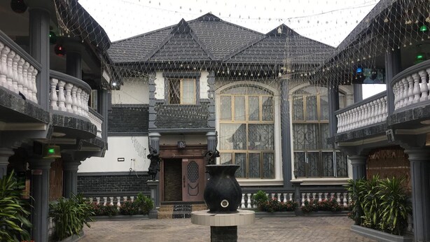 Ein Innenhof mit einer zentralen Fontäne, umgeben von einem Gebäude mit einem Ziegeldach und einem großen Fenster.