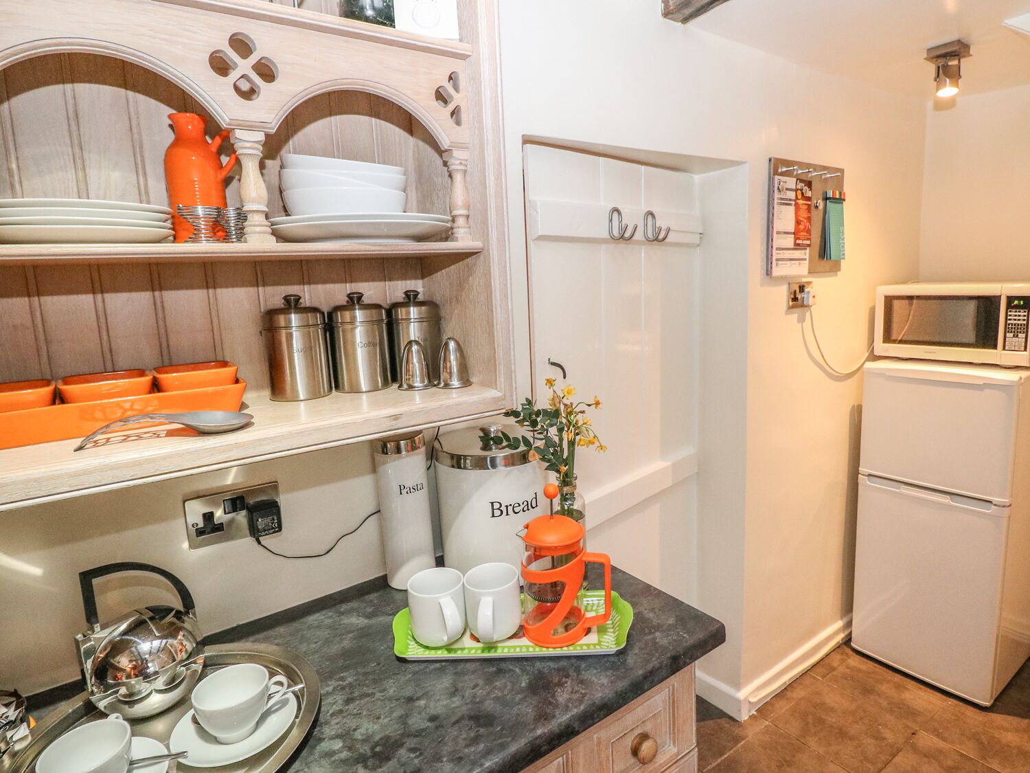 A kitchen with a microwave, refrigerator, and various kitchenware including cups, plates, and containers.