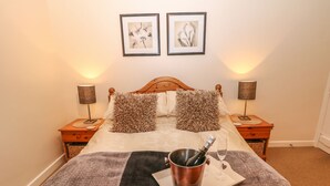 Une chambre à coucher bien rangée, avec un lit, deux lampes de chevet, une table de nuit, une tête de lit en bois et deux tableaux encadrés accrochés au mur.