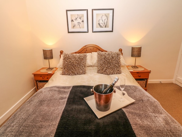 A neatly arranged bedroom with a bed, two bedside lamps, a nightstand, a wooden headboard, and two framed pictures on the wall. - Elderbank (Hope Valley)