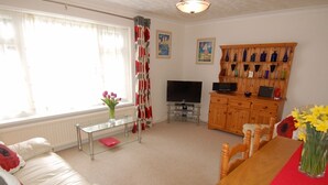 Un salon comprenant un canapé, une table basse, un téléviseur, un meuble en bois orné d’objets décoratifs et une fenêtre avec des rideaux.