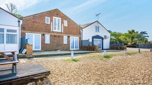 A residential area with two houses, one with a brick facade and the other with a white exterior. There is a wooden deck in the foreground and a gravel driveway. - Starboard (Yarmouth)