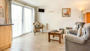 A spacious living room with a wooden coffee table, a cushioned armchair, and a sofa. A flat-screen TV is mounted on the wall, and a painting is visible. - Starboard (Yarmouth)