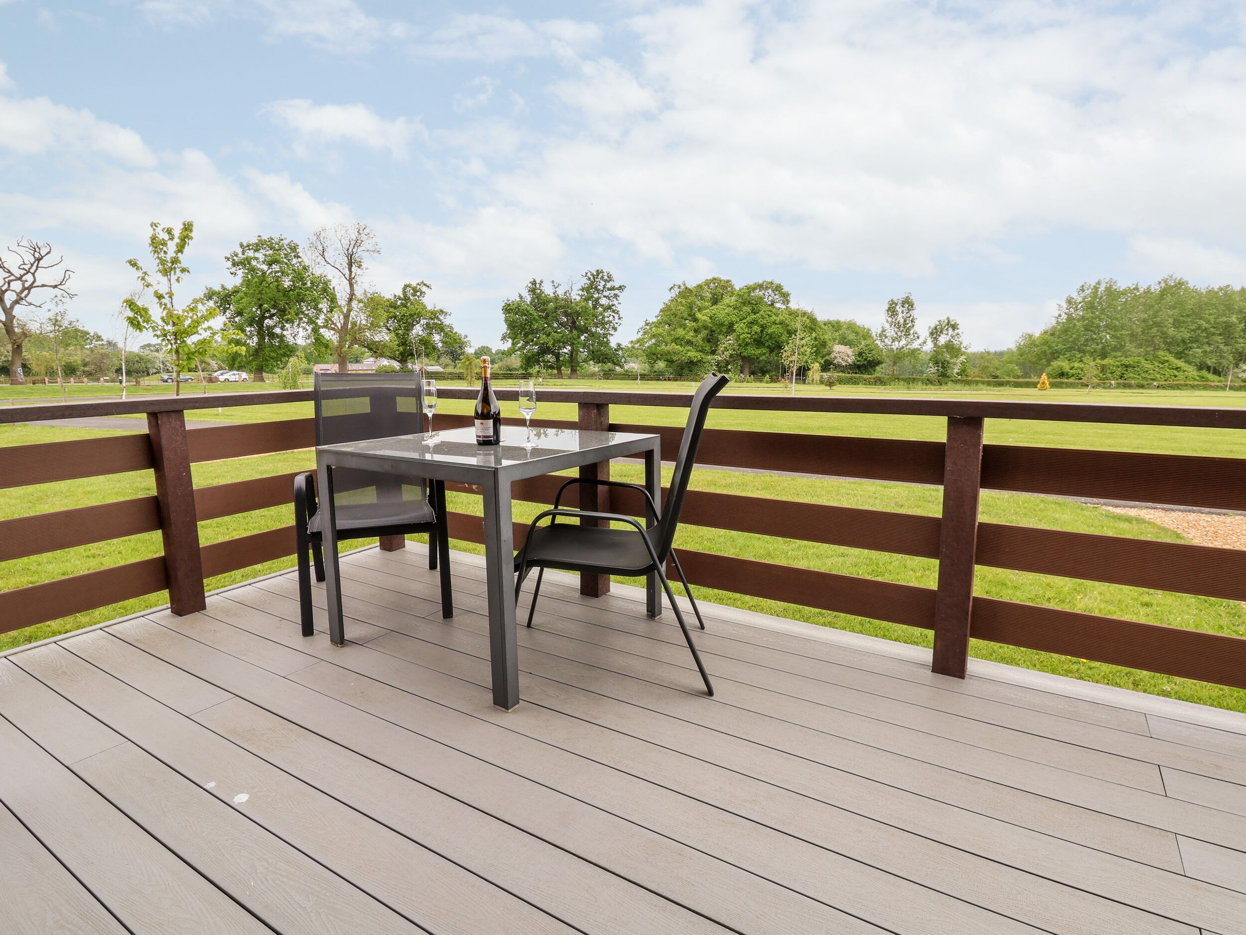 A deck with a table and chairs, overlooking a grassy area with trees.