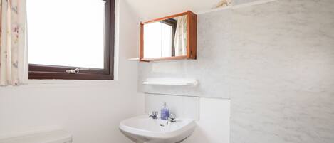 Een badkamer met toilet, wastafel, spiegel en raam.