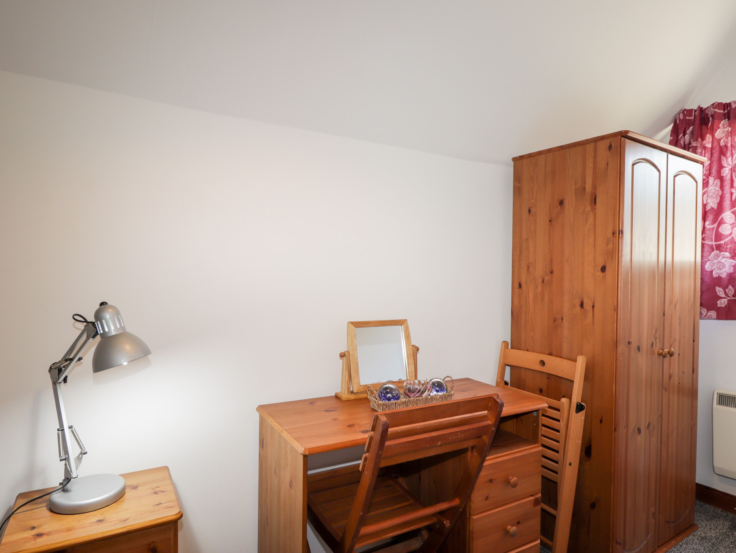Un bureau en bois avec une chaise, une lampe de bureau, un petit meuble en bois et un miroir.