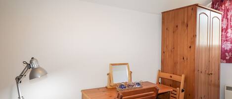 Un bureau en bois avec une chaise, une lampe de bureau, un petit meuble en bois et un miroir.