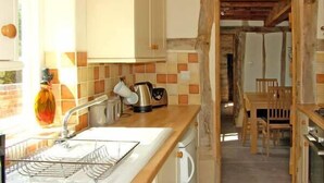 A kitchen with a sink, a kettle, and a coffee maker. There is a wooden table and chairs in the background. - Point Cottage (Hereford)