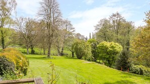 A well-maintained grassy area with a wooden bench, surrounded by various trees and shrubs. - Old Ford Farm Annexe (Axminster)