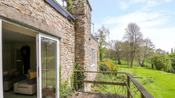 A stone building with a wooden deck and a glass door leading to a room with a sofa and a table. - Old Ford Farm Annexe (Axminster)