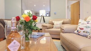 Una sala de estar con una mesa de centro de madera, una botella de prosecco orgánico y un florero con rosas.