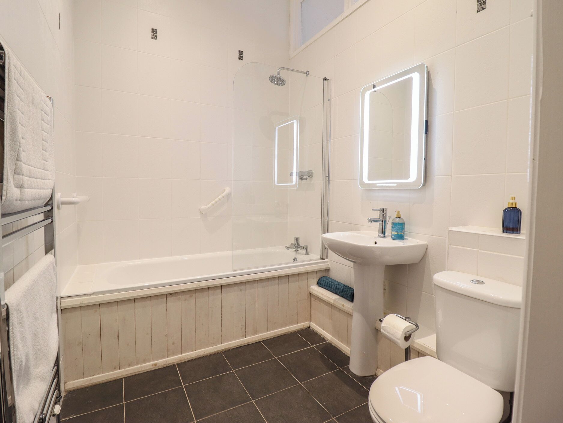 Et badeværelse med badekar, vask, toilet og bruser.
