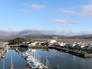 A marina with boats docked, surrounded by buildings and a mountainous backdrop.