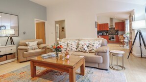 Una sala de estar con un sofá, una mesa de centro y una alfombra. Se ve una cocina al fondo con armarios y una zona de comedor.