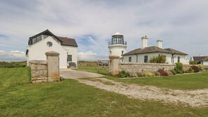 A coastal house with a lighthouse, stone walls, and a grassy lawn. - Old Higher Lighthouse Branscombe Lodge (Portland)