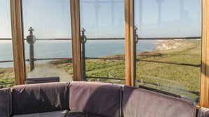 A panoramic view from a high vantage point, overlooking a coastal landscape with grassy areas and a body of water. - Old Higher Lighthouse Branscombe Lodge (Portland)