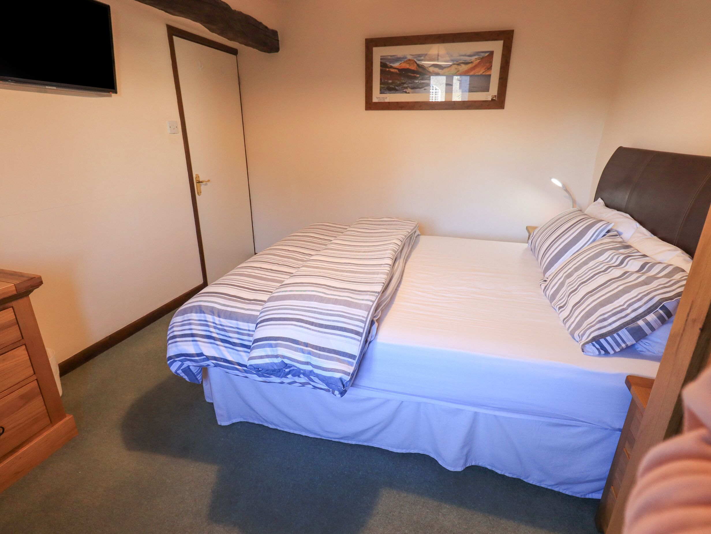 A bedroom with a bed, a wooden dresser, a painting on the wall, and a door.