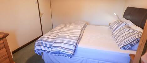 A bedroom with a bed, a wooden dresser, a painting on the wall, and a door.