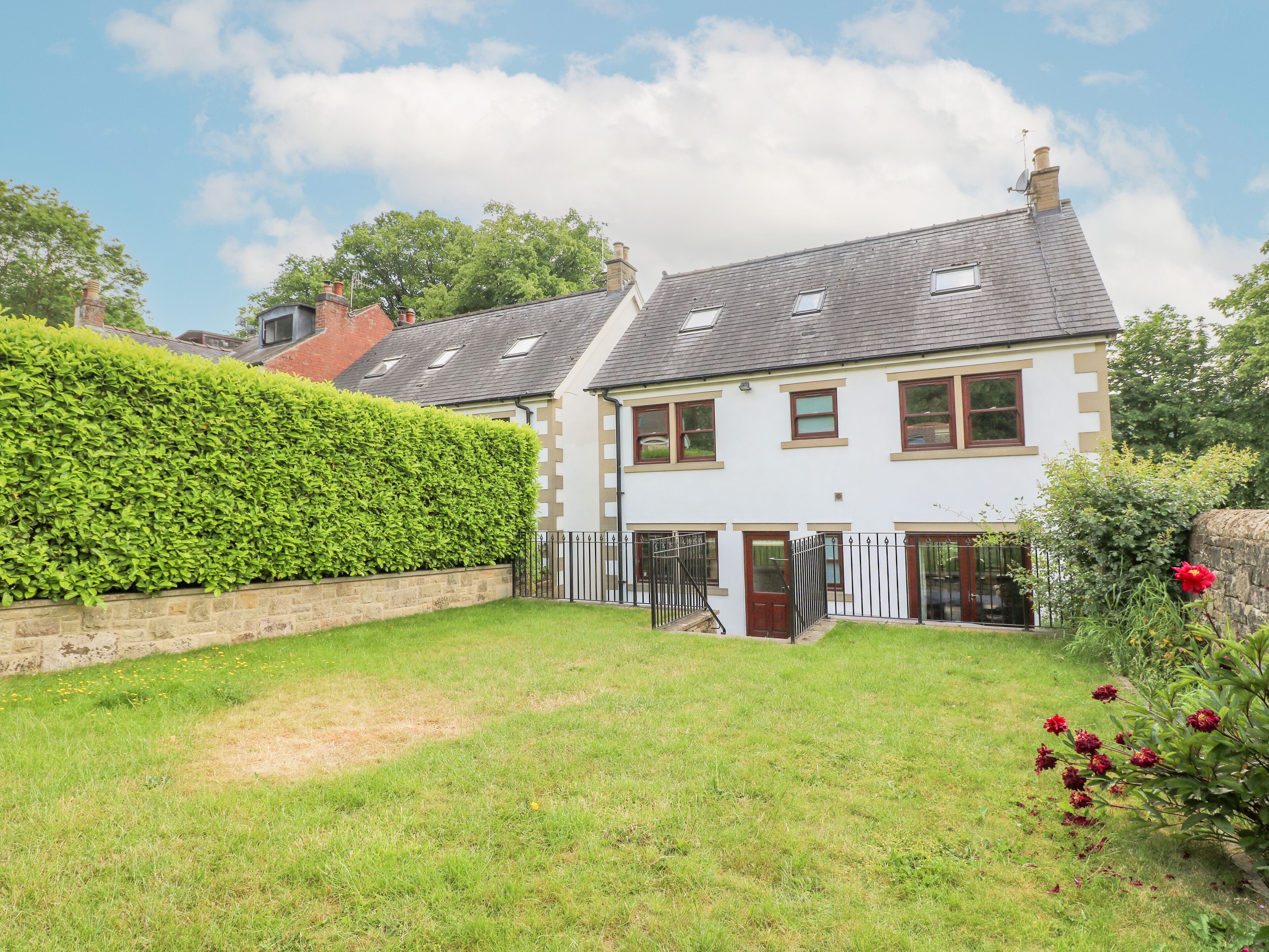 A two-story house with a well-maintained garden, a stone wall, and a red flower bush.