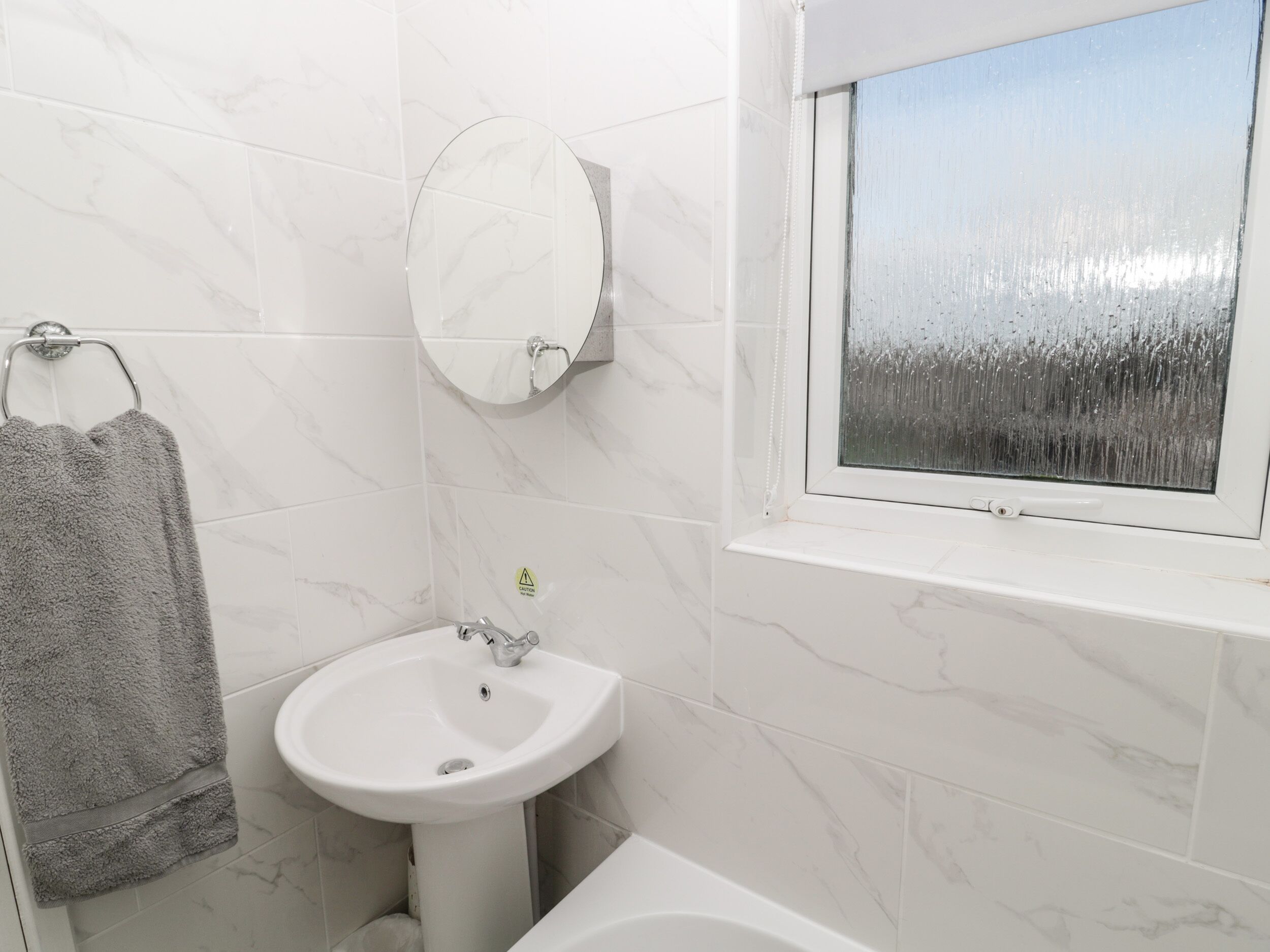 A bathroom with a white sink, a mirror, and a window with a view of trees.