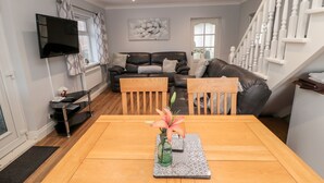 Un salon moderne avec une table à manger en bois, deux chaises, un téléviseur fixé au mur, un canapé et un escalier.