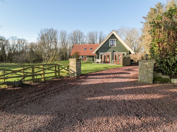 A green house with a red roof, a gravel driveway, and a wooden fence. - Apple Tree Lodge (Morpeth)
