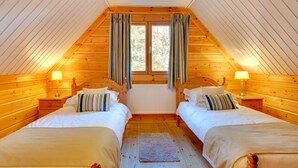 A cozy attic bedroom with two beds, wooden walls, and a window with curtains. - Apple Tree Lodge (Morpeth)