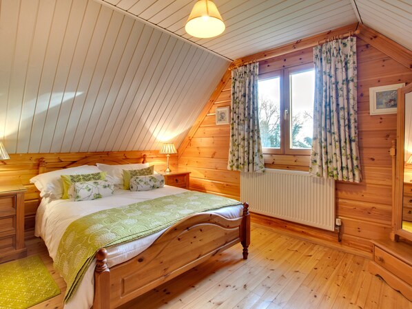 A cozy bedroom with a wooden bed, a window with floral curtains, and a radiator. - Apple Tree Lodge (Morpeth)