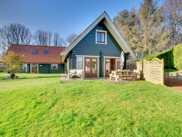 A two-story house with a sloped roof, a front porch with a table and chairs, and a well-maintained lawn. - Lime Tree Lodge (Morpeth)