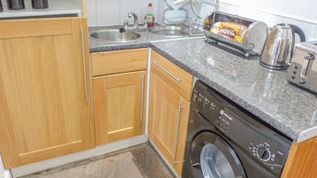 Cocina compacta con armarios de madera, lavadora, tostadora y pileta.