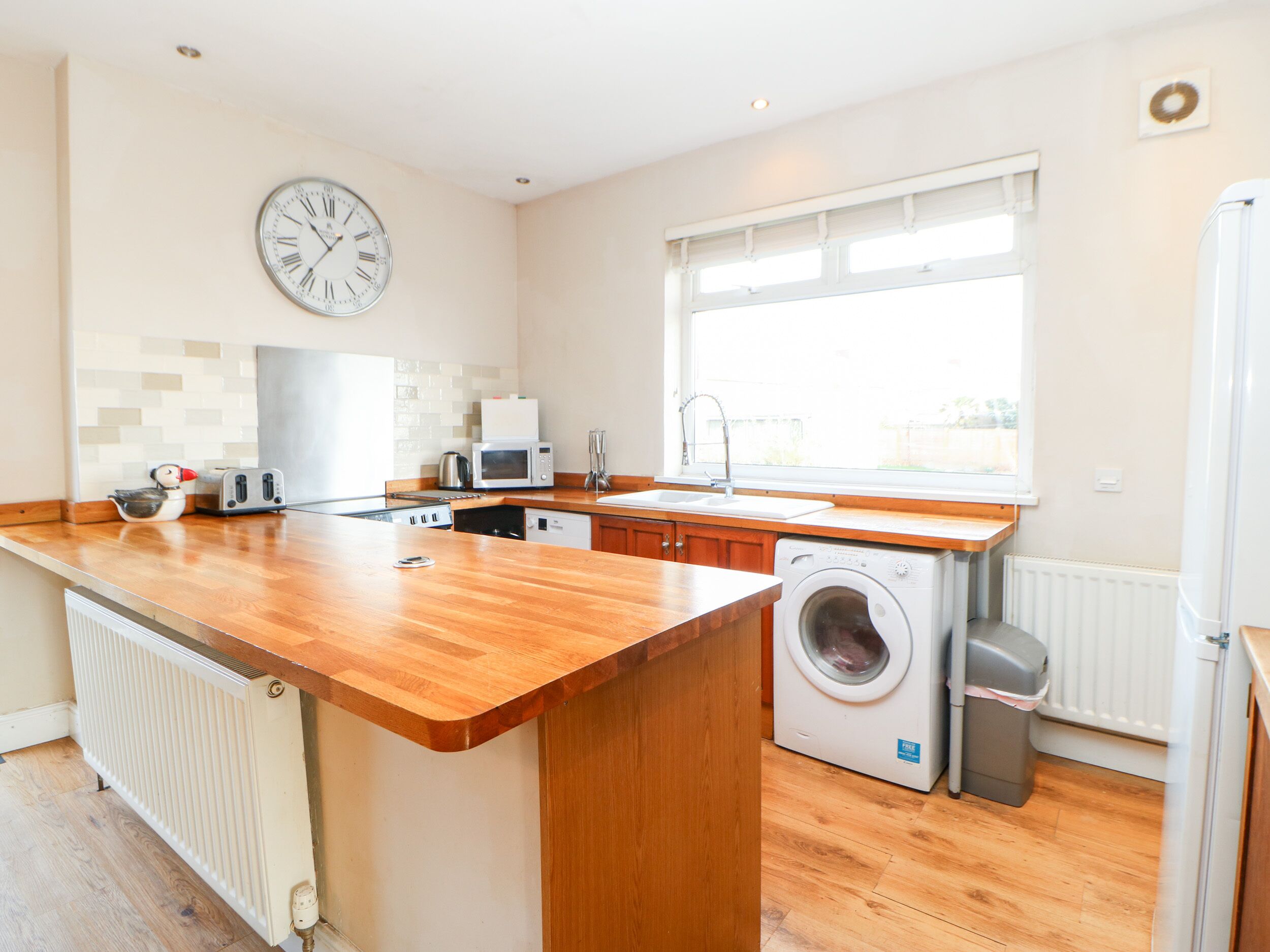 Een moderne keuken met houten aanrecht, een ingebouwde wasmachine, een magnetron en een spoelbak.