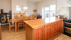 A kitchen with wooden cabinets, a central island, and a dining area with chairs. - Lightkeeper House (Morpeth)