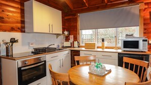 Cucina di una baita in legno con fornello, lavello, forno a microonde e un tavolo da pranzo con sedie.
