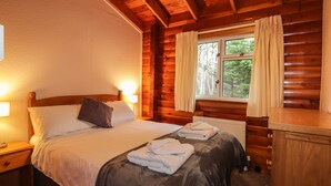Una camera da letto in una baita di legno, con un letto di legno, due comodini, una finestra con tende e un termosifone.