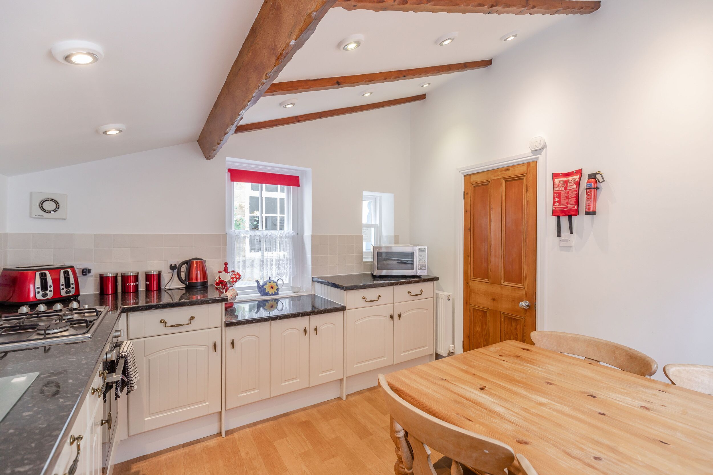 A kitchen with white cabinets, a wooden table, a stove, a microwave, and a red fire extinguisher.