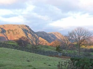 Paisaje rural con muro de piedra, campos de hierba y montañas al fondo.