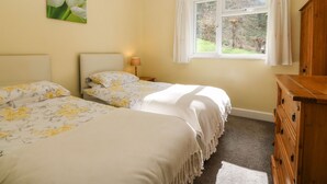 Un dormitorio con dos camas, una ventana con cortinas, una lámpara y un aparador de madera.