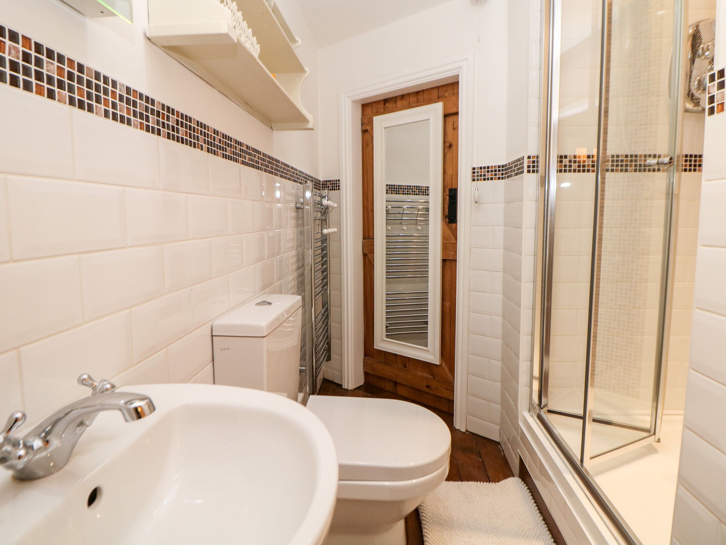 Une salle de bain avec des carreaux blancs, un lavabo, des toilettes et une douche à parois de verre.