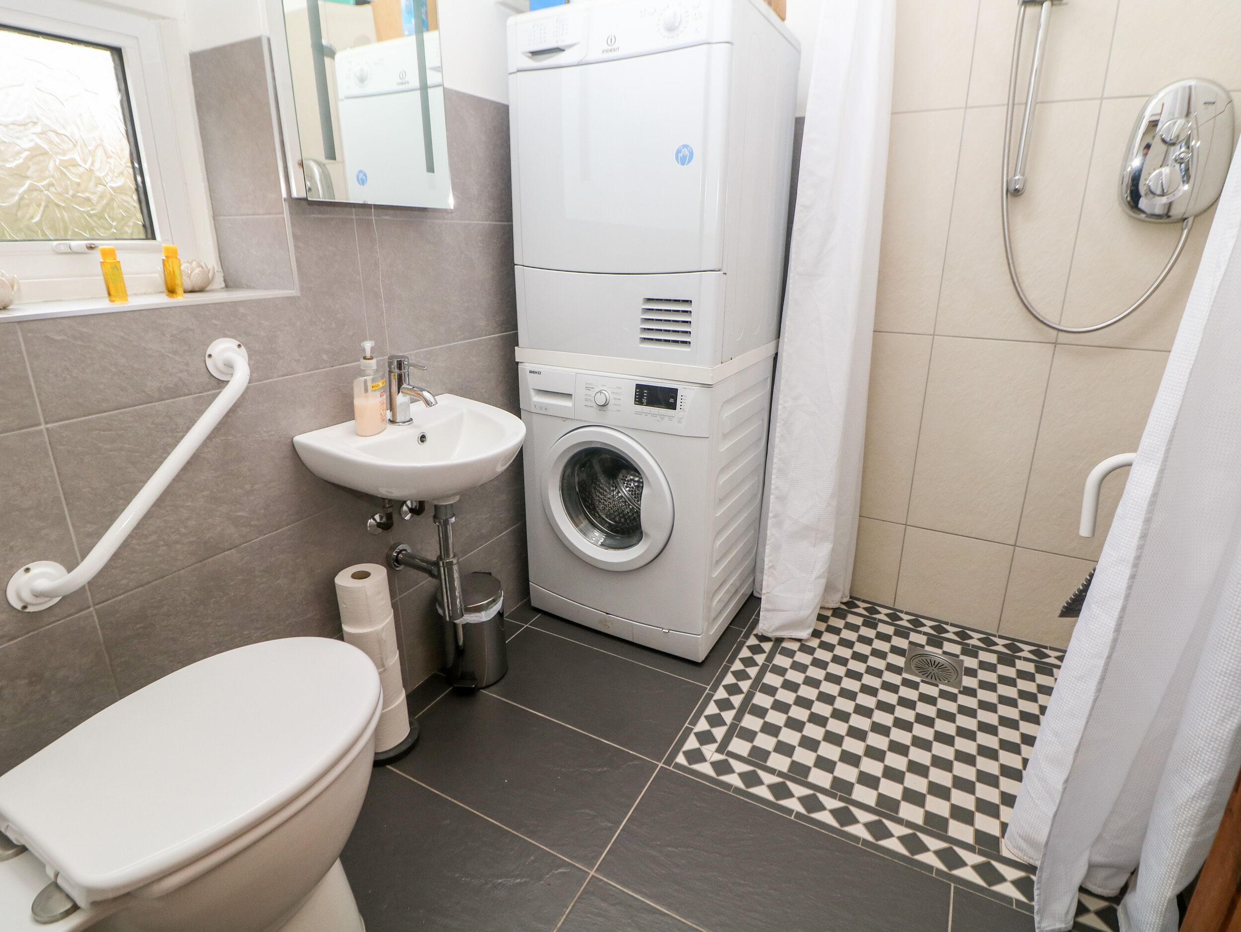 A bathroom with a toilet, sink, washing machine, and shower.