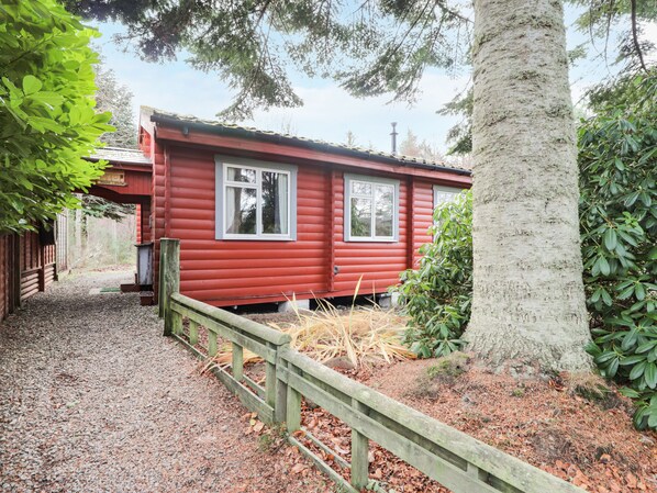 Situated in a wooded area, this cabin features a rustic exterior with a gravel path leading to the entrance.