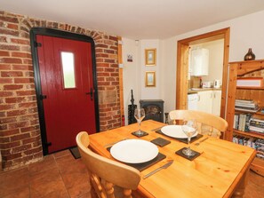 A dining area with a red door, brick walls, a fireplace, and a bookshelf. - Top Stable Cottage (Belper)