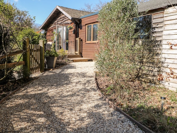 A wooden house with a gravel driveway leading to a wooden gate. - Woodmancote Lodge (Haslemere)