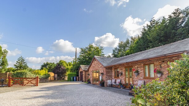 A brick building with a gravel driveway, a wooden gate, and outdoor seating. - Wild Duck Lodge (Ormskirk)